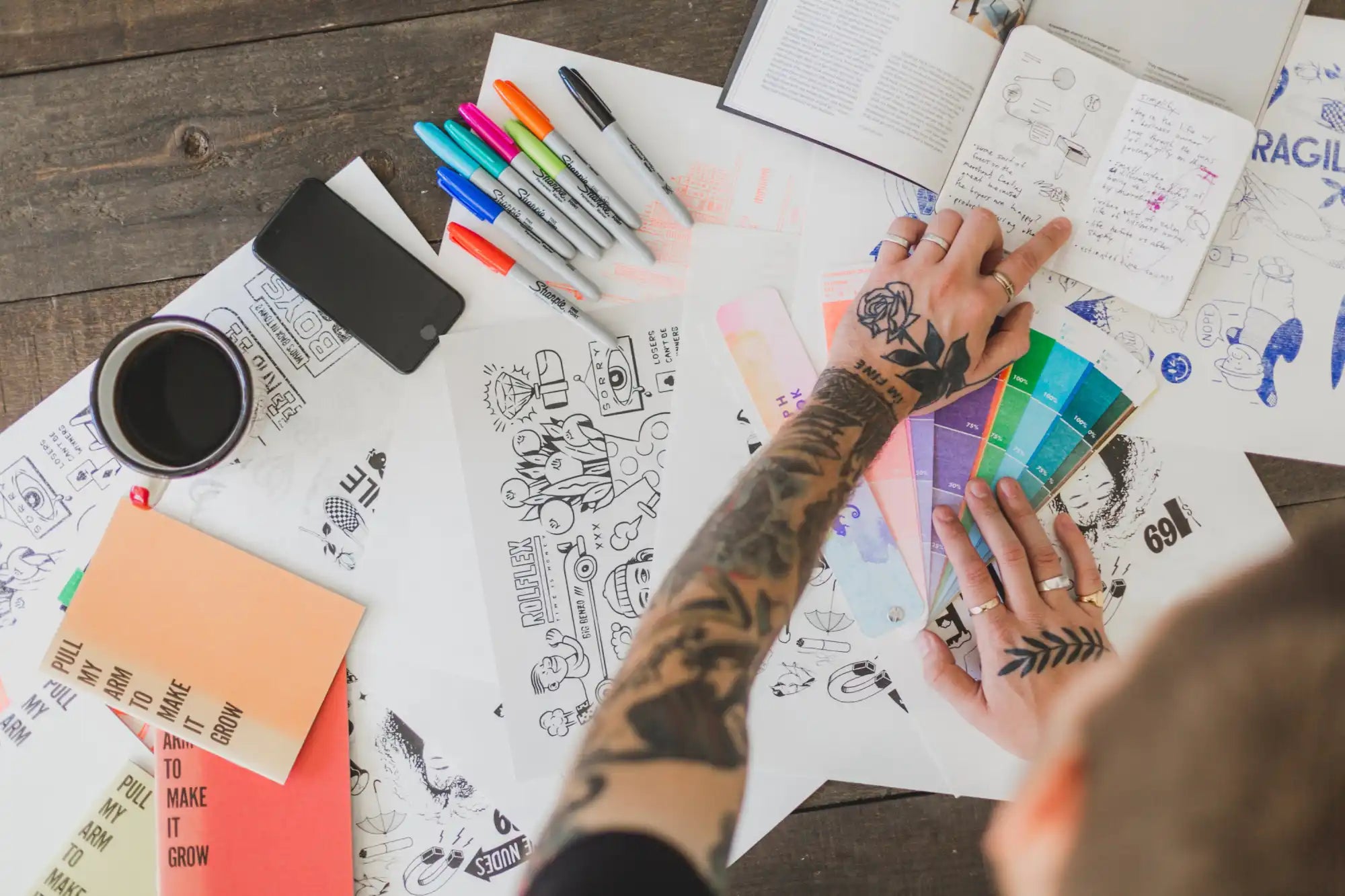 Tattooed hands holding color swatches.